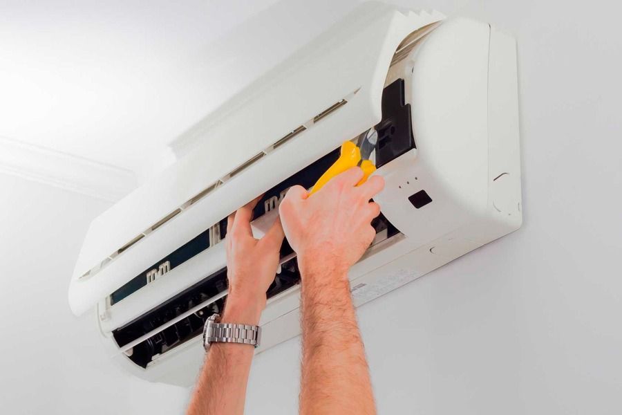 Manos limpiando un aire acondicionado blanco montado en la pared con un pa&ntilde;o amarillo.